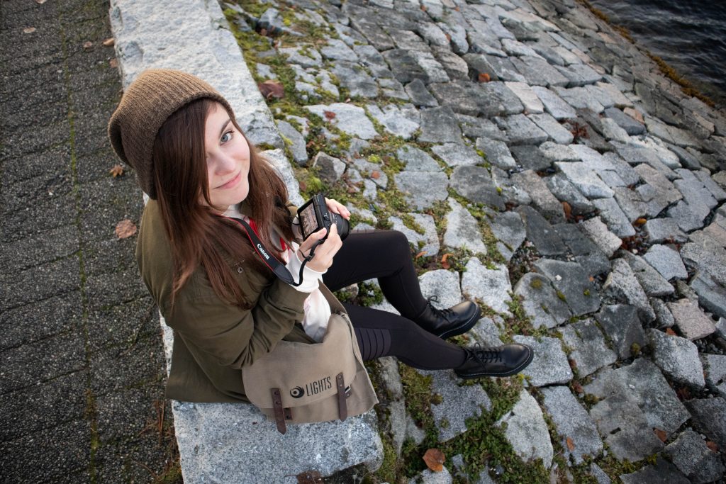 Briana sitting on a rocky garden wall holding her camera
